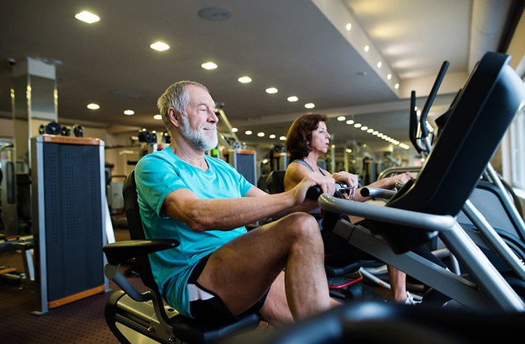 elderly man and woman riding recumbent bikes indoor