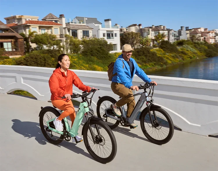man and woman riding two velotric electric bikes over a bridge