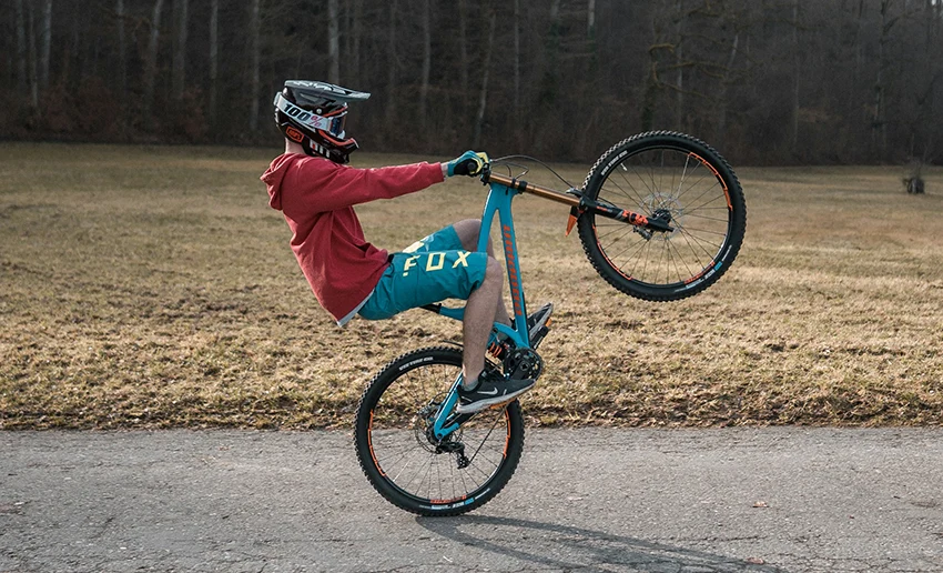 mountain biker doing a wheelie while wearing full mountain biking gear