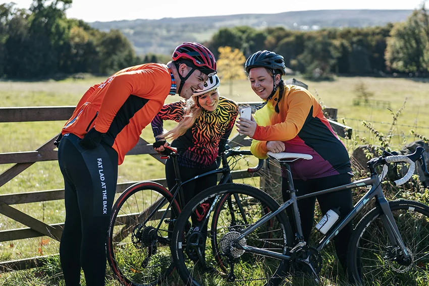 three cyclists reading bike jokes on a smartphone