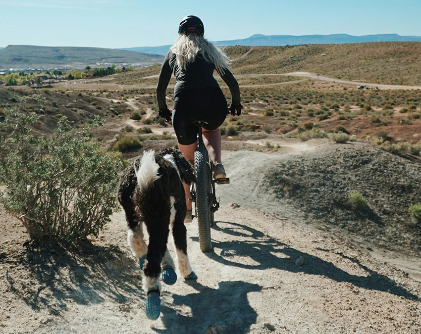 girl cycling with a dog in the desert