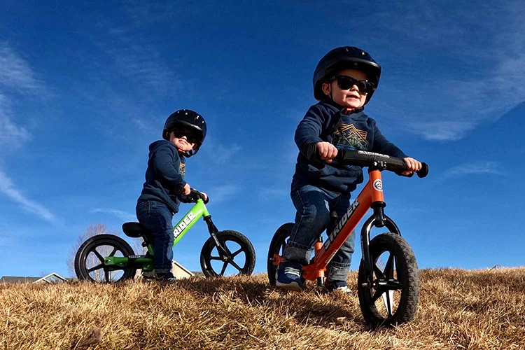 two toddler boys with sunglasses posing on strider balance bikes