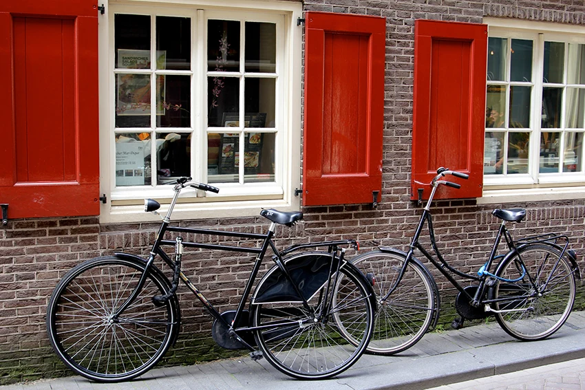two dutch style bikes leaned against a brick house with red window shutters